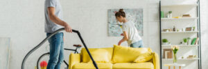 A man and woman cleaning- the man is vacuuming.